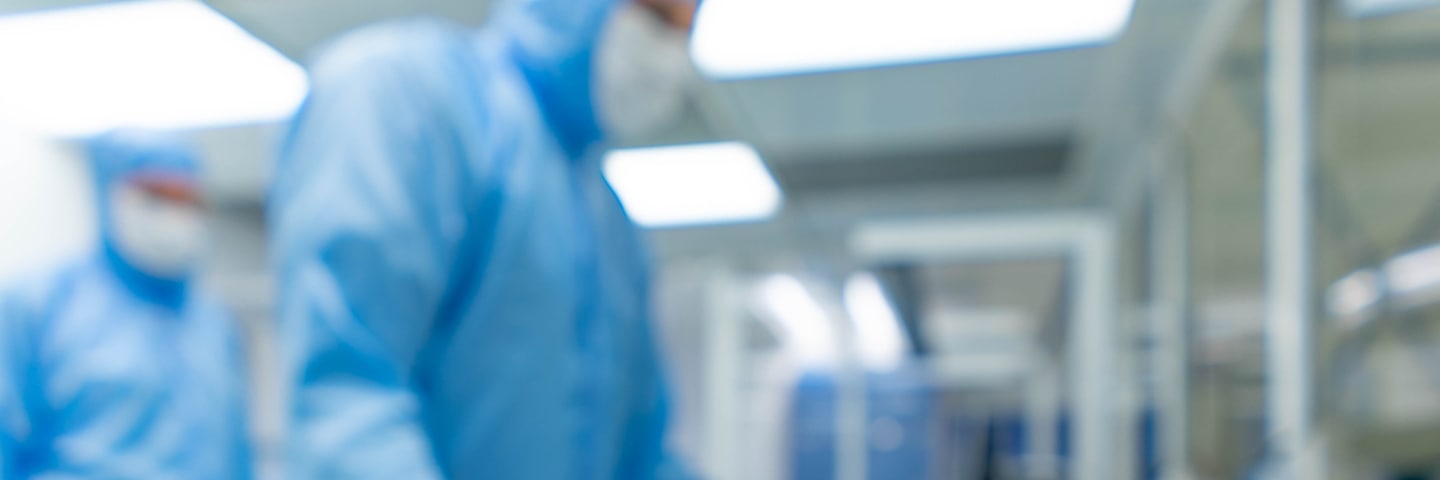 Employees in blue cleanroom suits next to a roll of yellow cleanroom labels