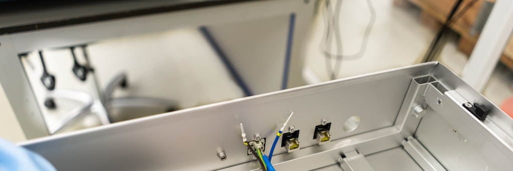 Gloved hands connect wires in a sheet metal enclosure