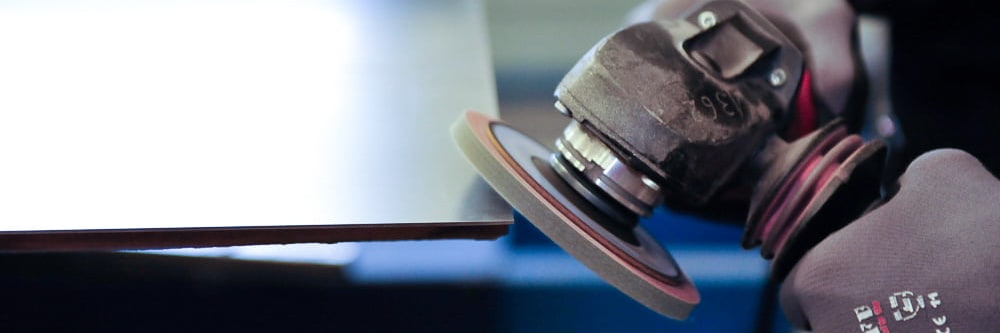 Gloved hand grinding the edge of a metal sheet with an angle grinder
