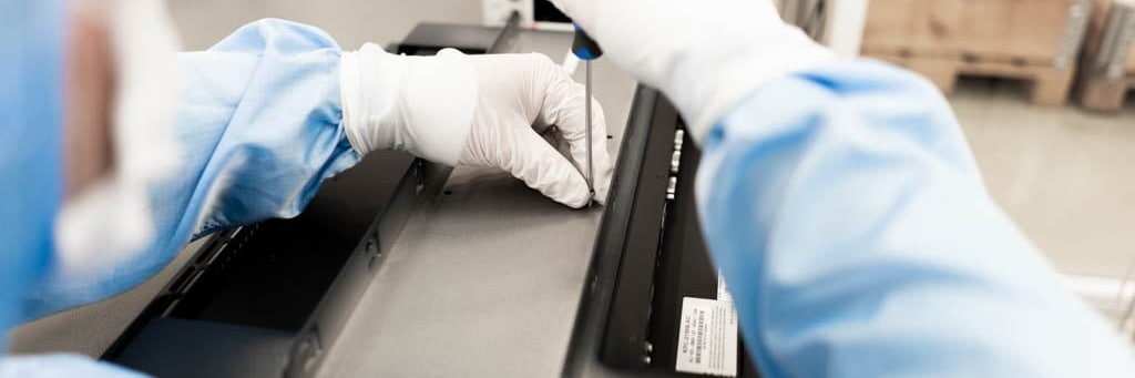 Hands in white gloves and cleanroom clothing screw together a black metal enclosure