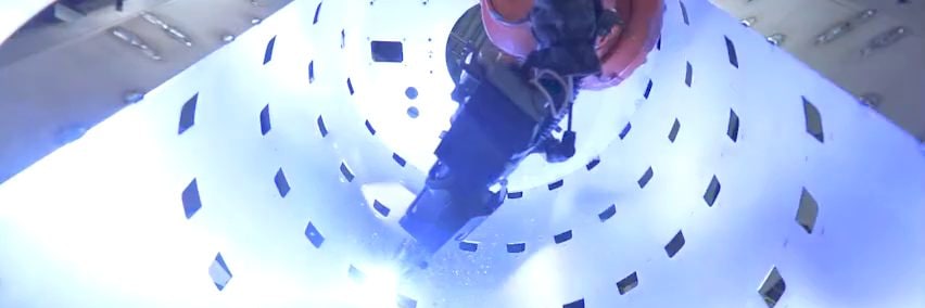 Schweißroboter schweißt ein Blech mit rechteckigen Aussparungen, mit hellblauem Lichtbogen