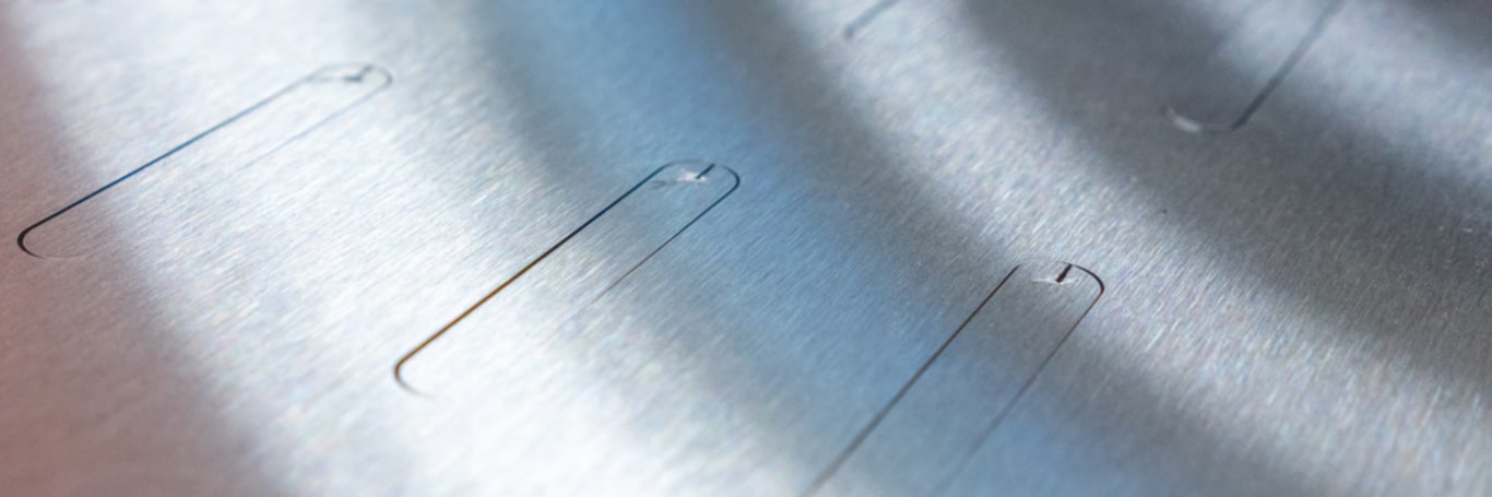 Close-up of brushed metal with cut-out slot-shaped inner contours