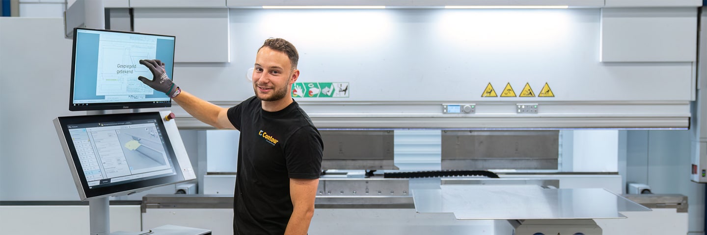 Contour employee pointing at a drawing on the screen of a CNC press brake, a sheet lies ready