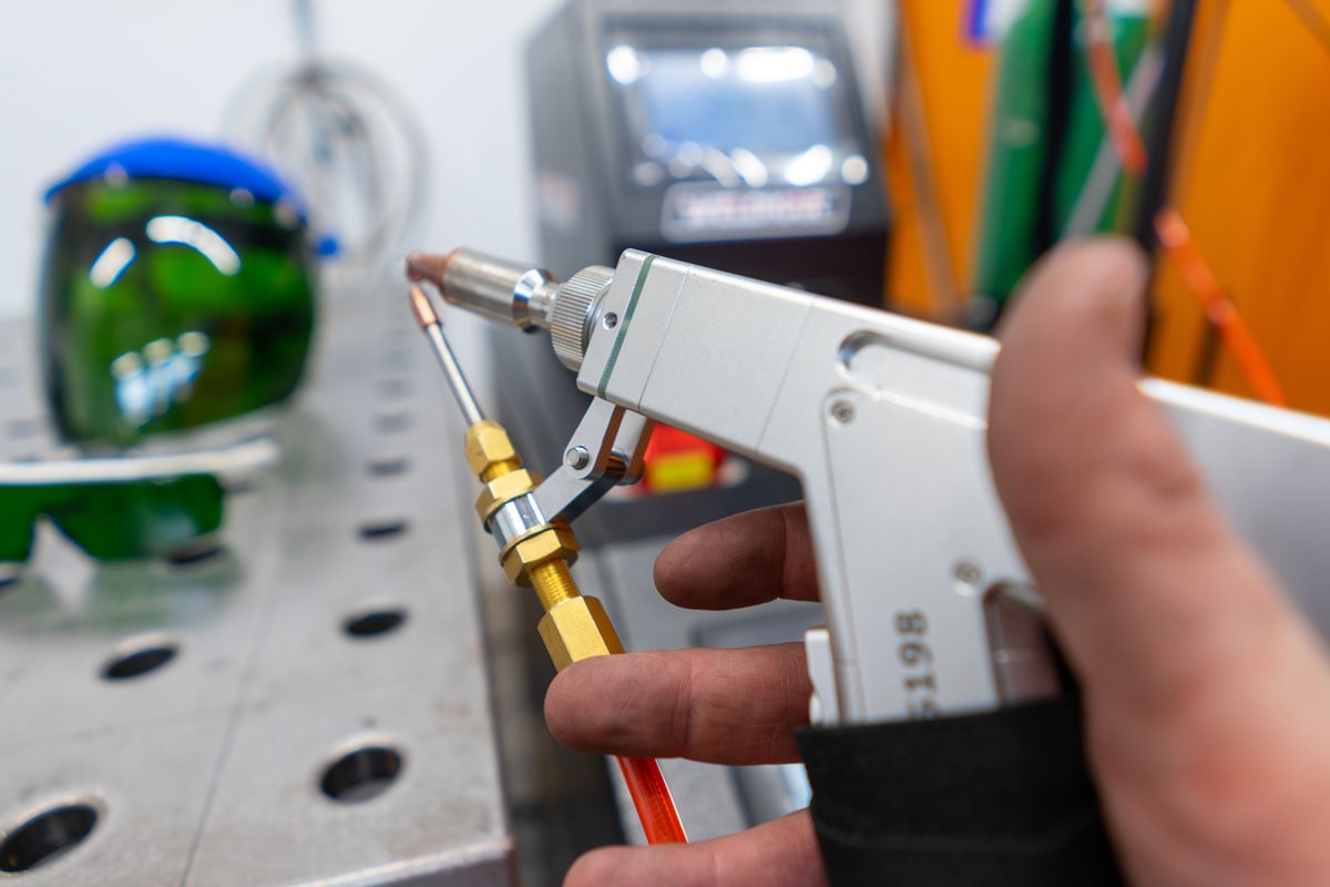 Hand met een handlaserlasapparaat naast een lasbril en een lastafel