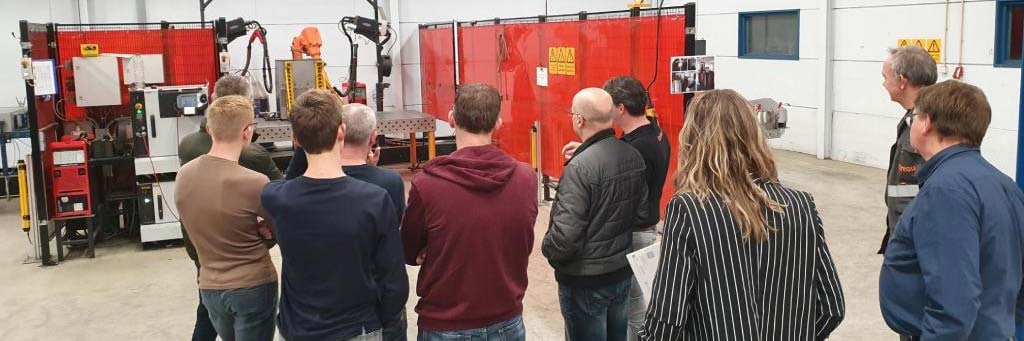 Besuchergruppe schaut bei einer Betriebsführung in der Werkstatt einem Schweißroboter zu