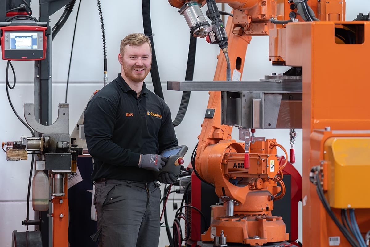 Operator met handbediening naast een oranje lasrobot