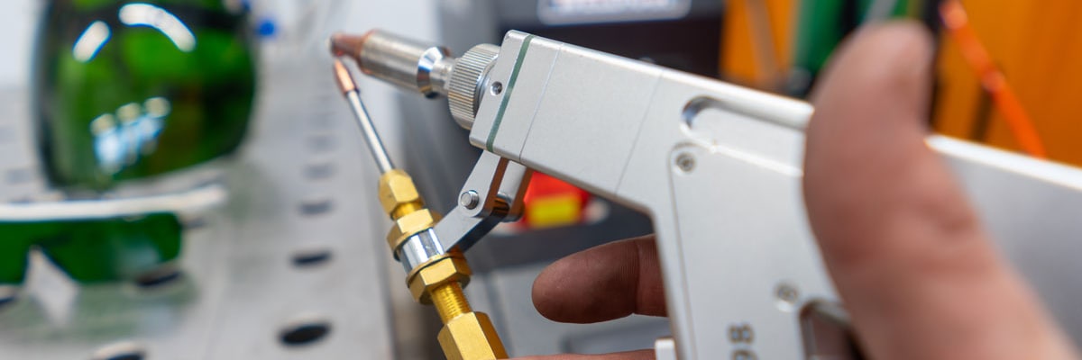 Hand holding a handheld laser welding device, with protective goggles and a welding table