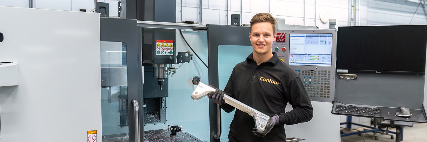 Employee holding a milled metal part in front of a Haas CNC milling machine