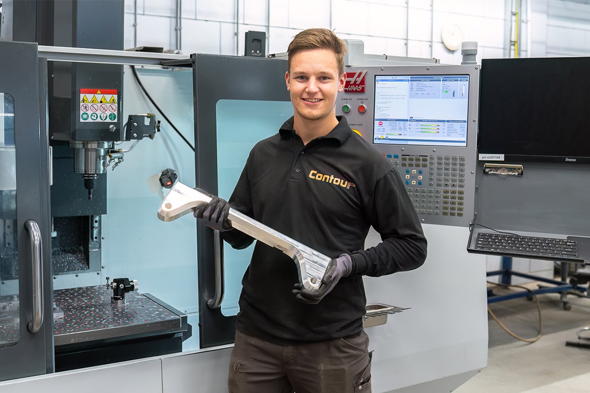 Medewerker houdt een gefreesd metalen onderdeel vast voor een Haas CNC-freesmachine