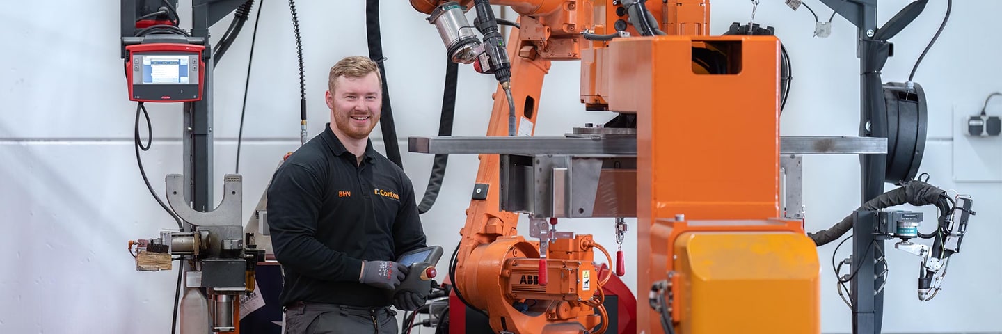 Bediener mit Handbediengerät neben einem orangefarbenen Schweißroboter