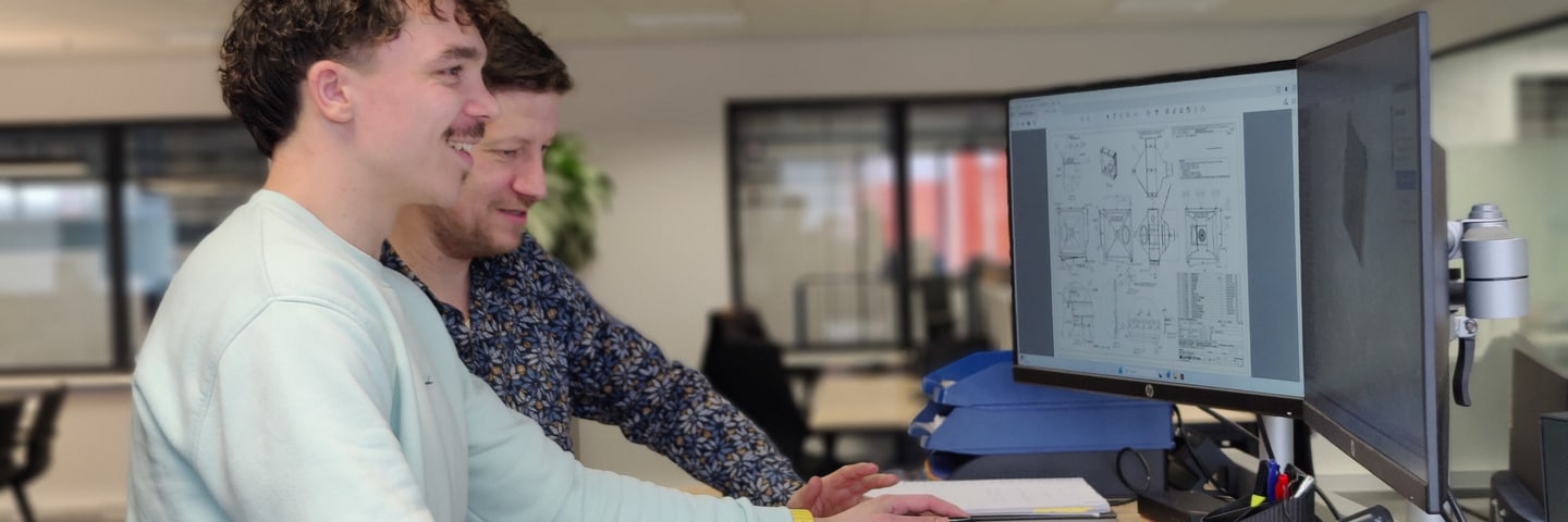 Two colleagues look at a technical drawing on a screen in the office