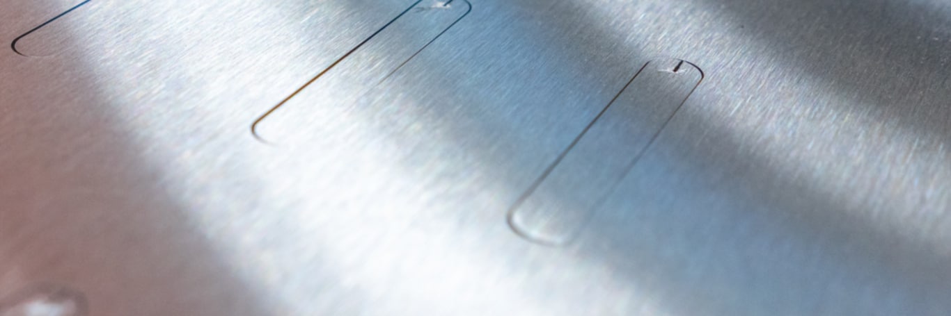 Close-up of brushed metal with cut-out slot-shaped inner contours