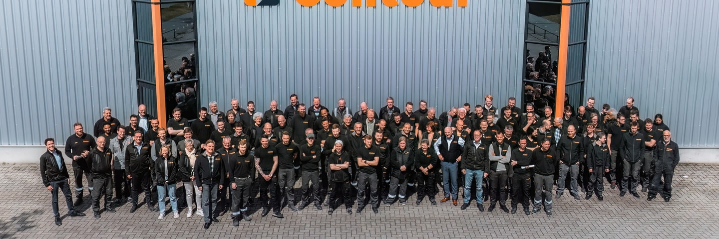 A large group of Contour colleagues pose in front of the facade with the Contour logo