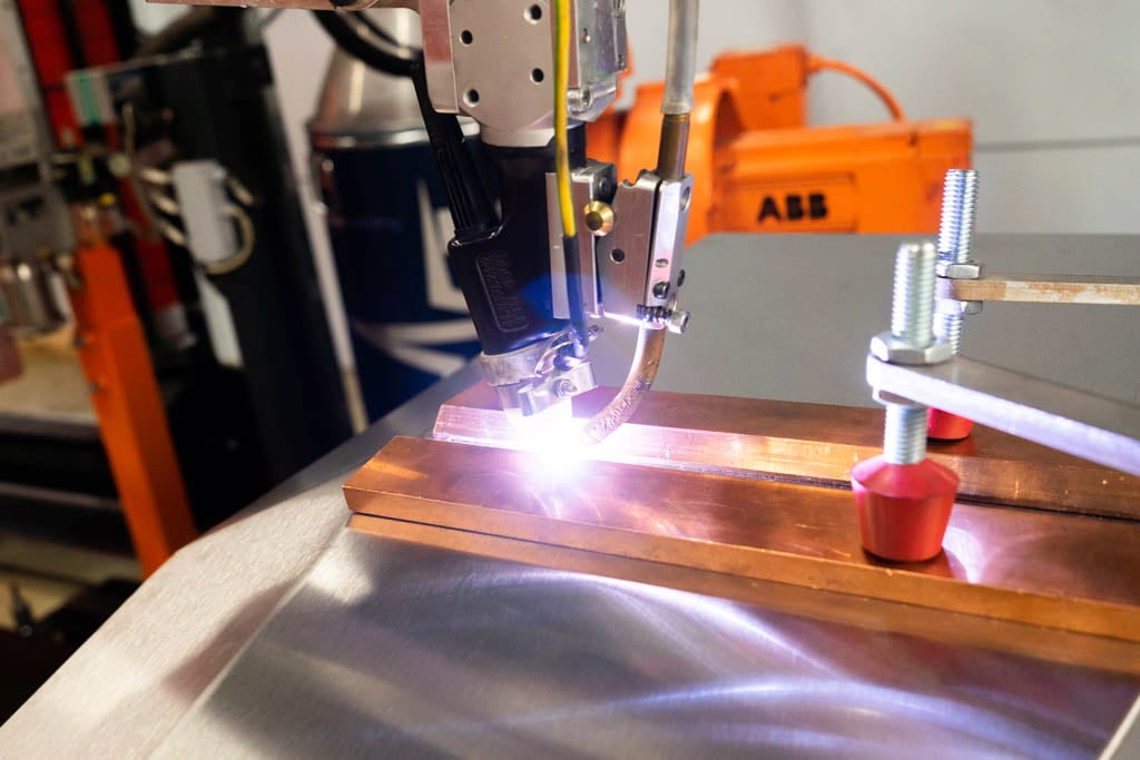 Welding robot torch welding along a copper strip on a metal sheet