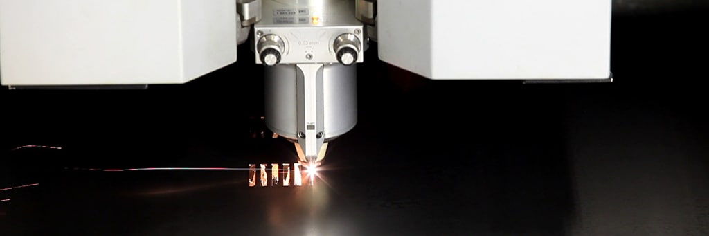 Laser head cutting a sheet, with a bright spot and sparks at the cut