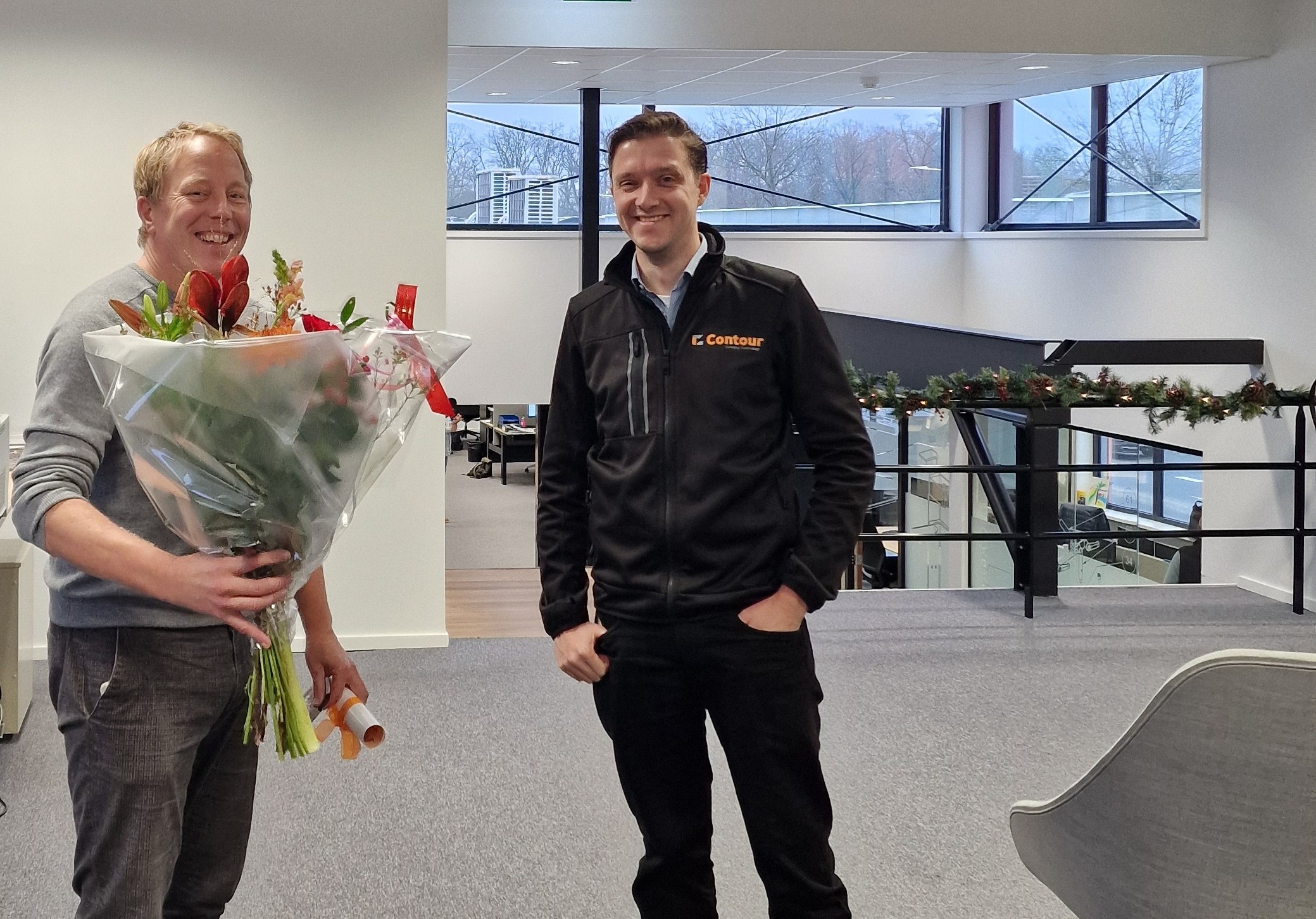 Jeroen viert zijn 12,5-jarig jubileum bij Contour, met een boeket bloemen naast een collega in een Contour-jas