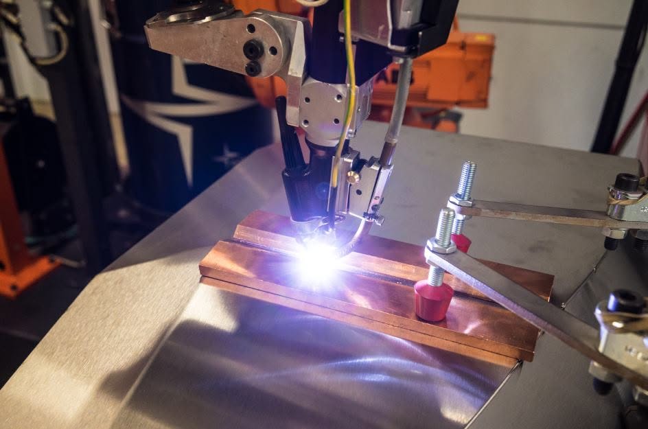 TIG-lastoorts van de ABB lasrobot last een plaatwerkdeel op een koperen onderlegstrip