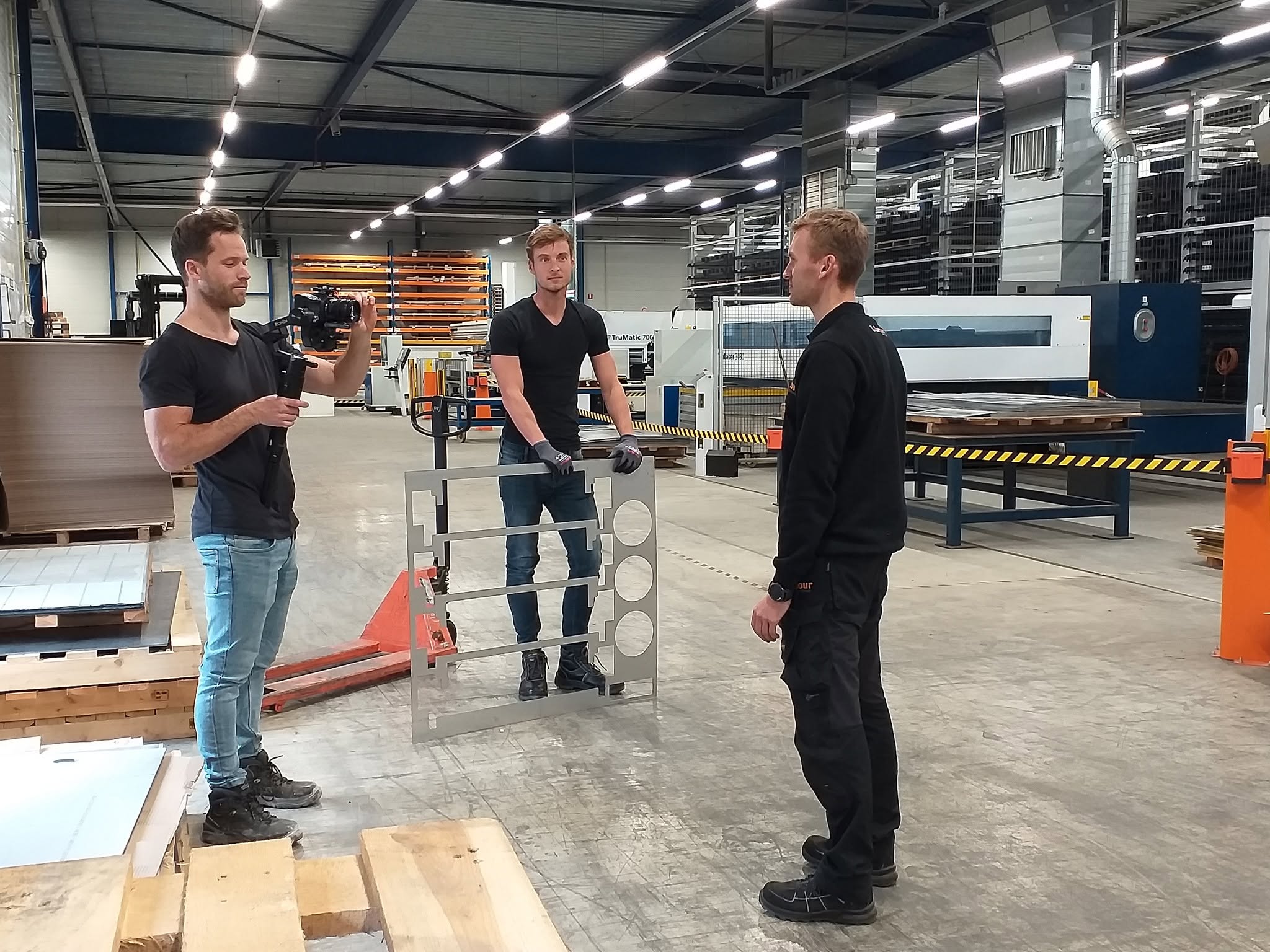 Een cameraman filmt een collega met een gelaserd plaatwerkdeel in de productiehal