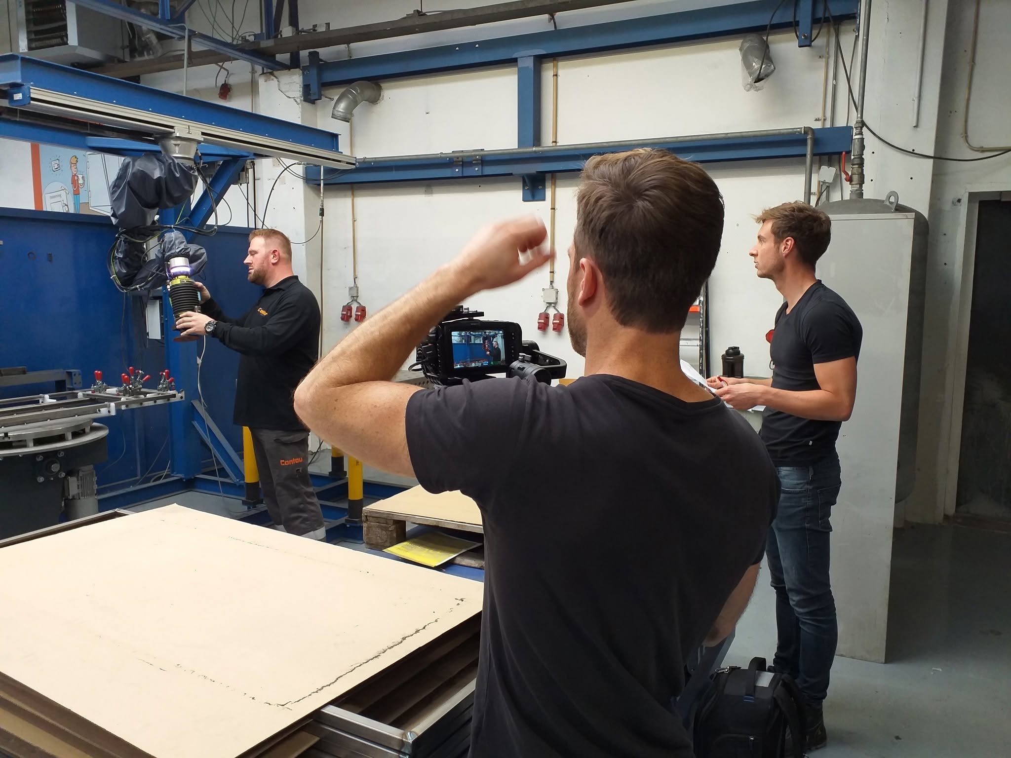 Een collega houdt een onderdeel vast bij een robotcel terwijl de cameraman filmt