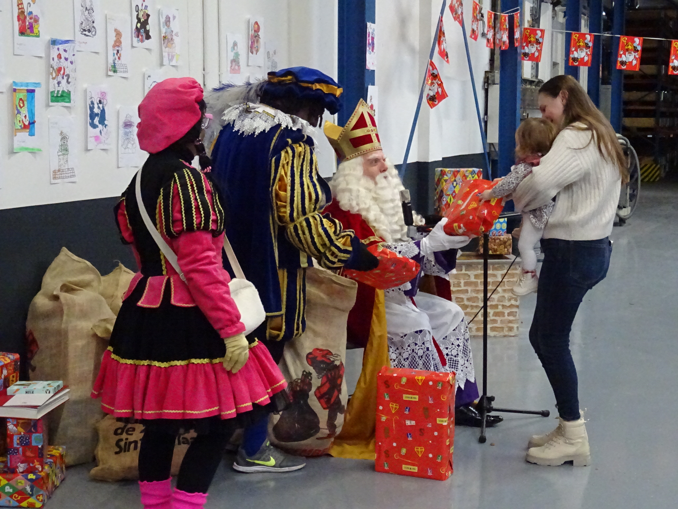 Sinterklaas en pieten delen cadeaus uit aan een kind in de productiehal