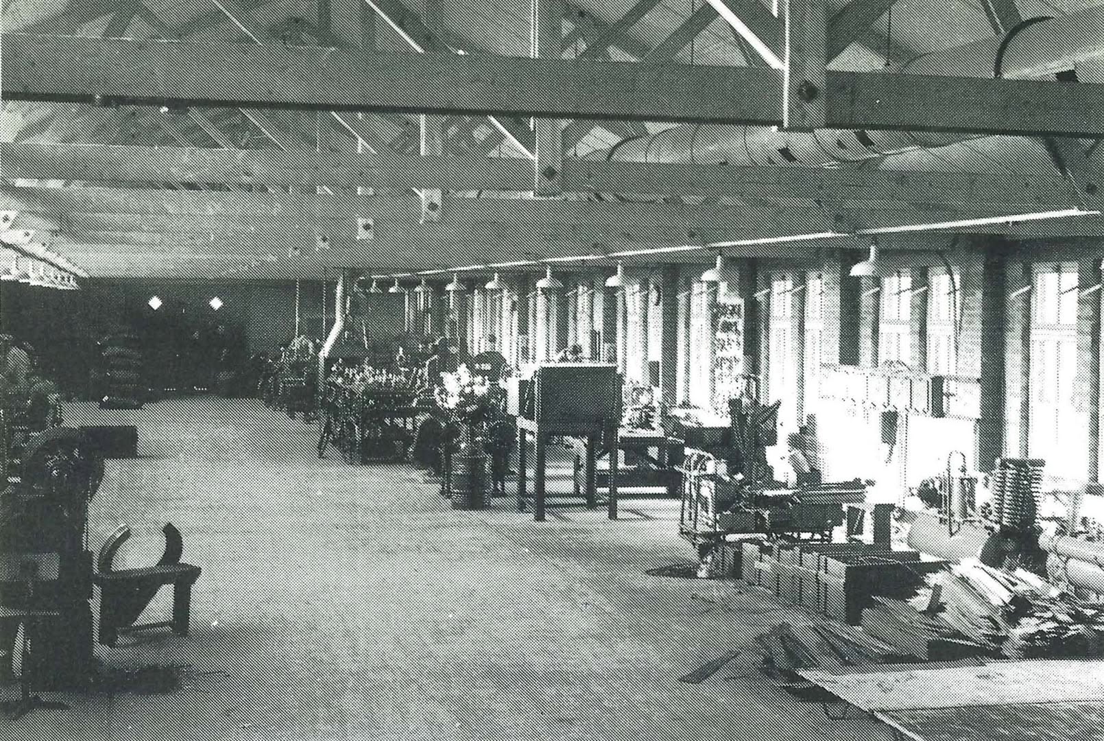 Zwart-witfoto van de oude productiehal met houten dakspanten en werktafels