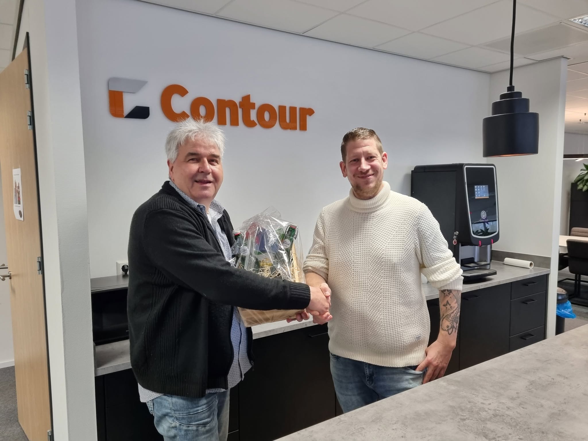 Wim krijgt een cadeaumand overhandigd van een collega voor het Contour-logo
